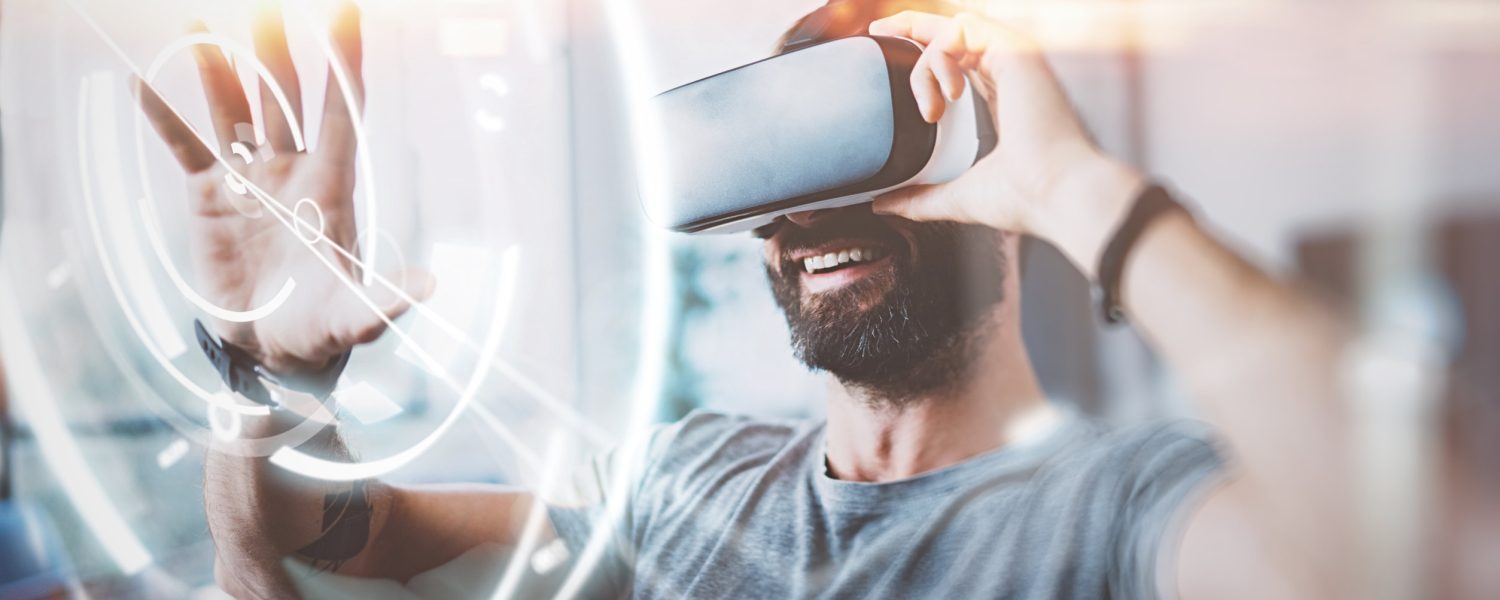 Concept of digital screen,connection and interfaces.Beraded hipster enjoyingvirtual reality glasses in modern design home studio.Smartphone use with VR goggles headset.Horizontal,flare,blurred